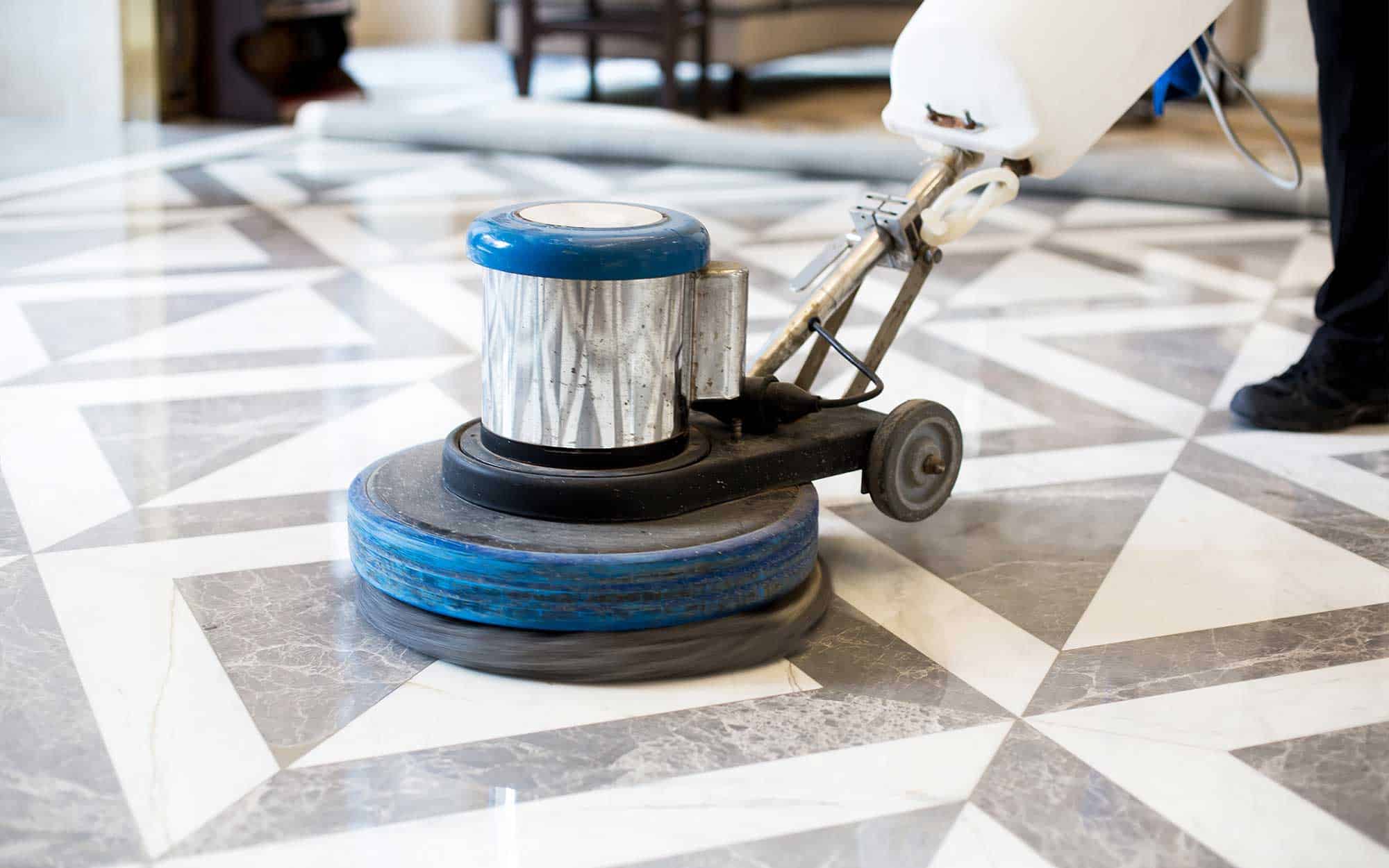 A person is using a floor polishing machine on a marble floor inside a building.