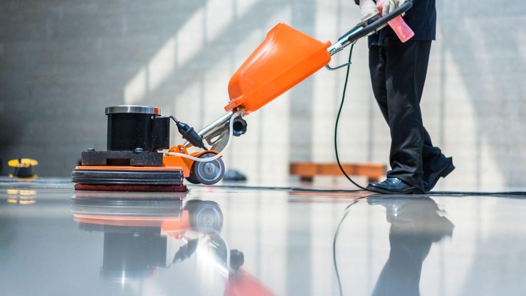 A person is mopping the floor of a kitchen, wearing gloves and casual attire.